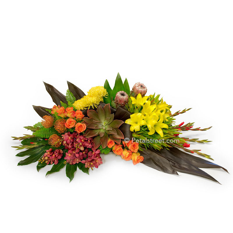 Tropical style casket spray with King Protea, orange Roses, red Orchids, Succulents, and lush green leaves.