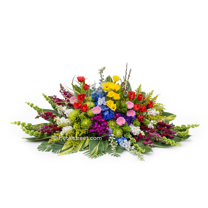Spring garden casket spray with mixed seasonal flowers such as Tulips, Daffodils, Snapdragons, accent grasses and greenery.