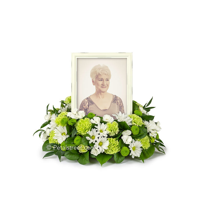 Cremation flower arrangement with tribute photo frame in center includes Daisies, Carnations, Dianthus, Button Mums, and accent foliage.