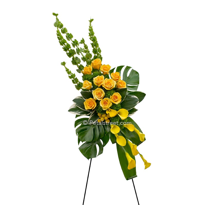 Gorgeous standing spray of funeral flowers, yellow Roses & Calla lilies with large monstera leaves.