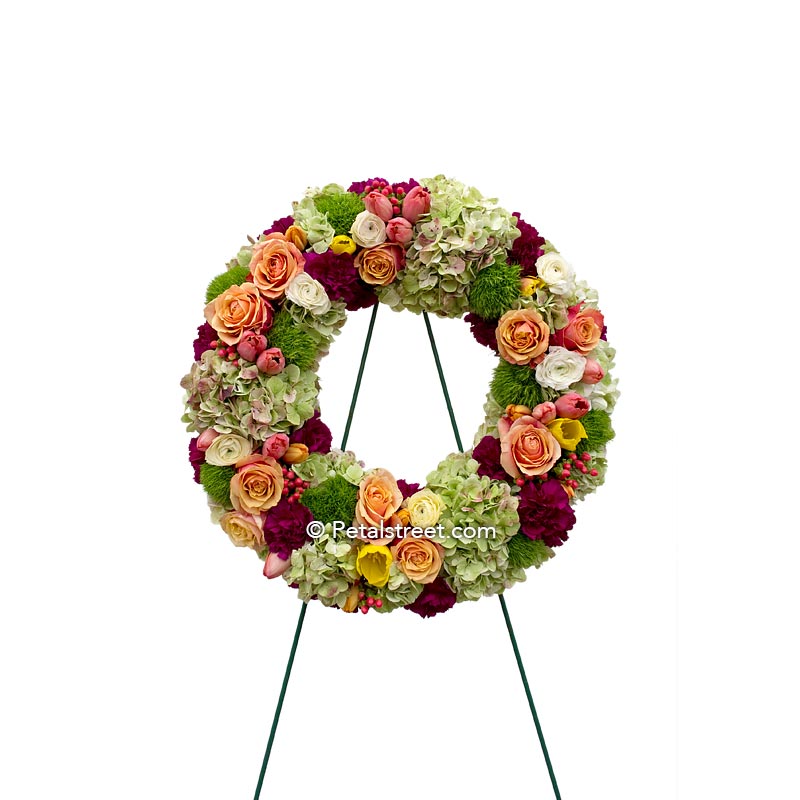 Beautiful funeral wreath in soft oranges and greens with Roses, Carnations, Hydrangea, and mixed accents.