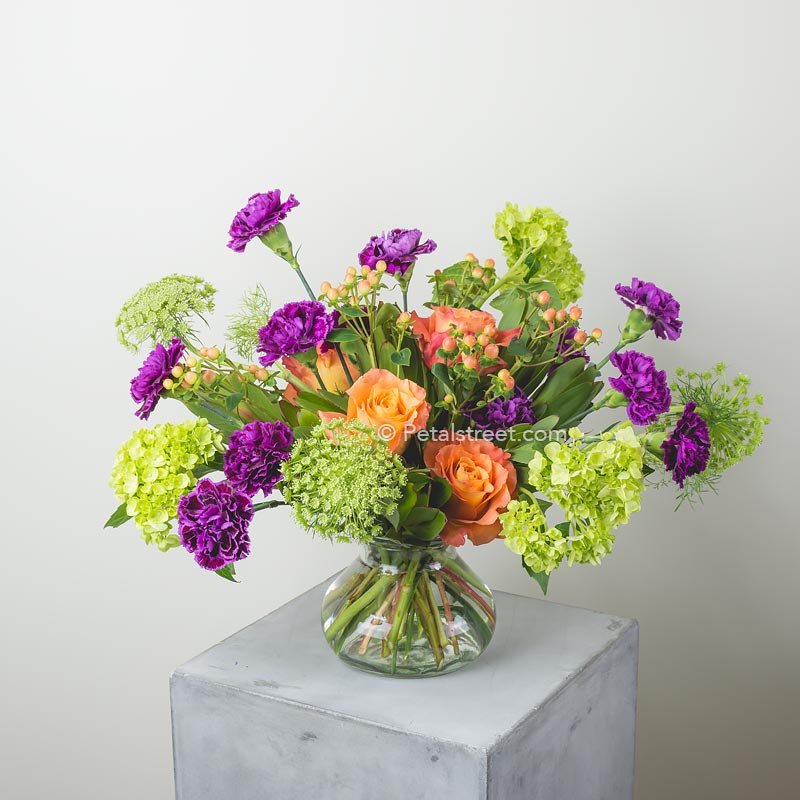 Vibrant mixed flower arrangement with orange Roses, purple Carnations, green Hydrangea, Lace flower, and Hypericum Berry accents by Petal Street Flower Company florist in Point Pleasant NJ