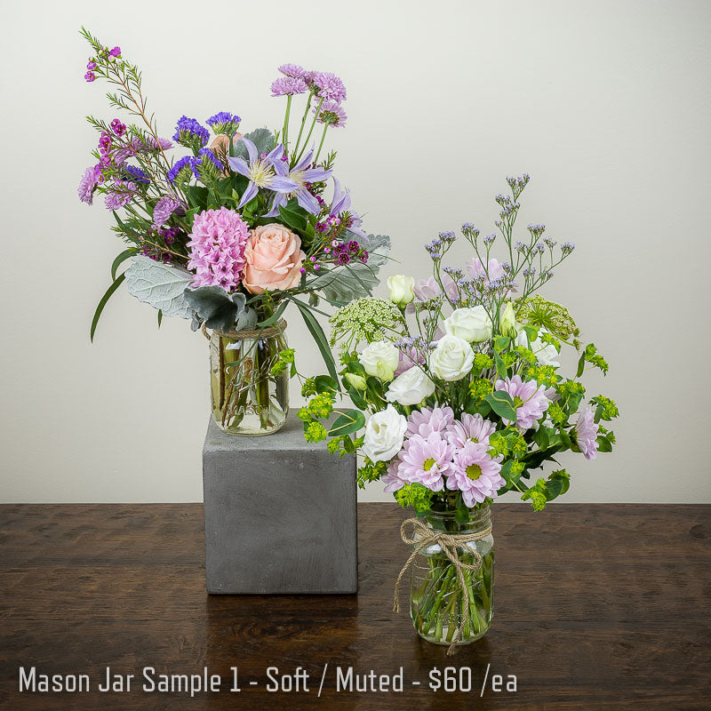 A pair of soft colored mason jar flower arrangements with peach lavender, and white blooms and accent greenery