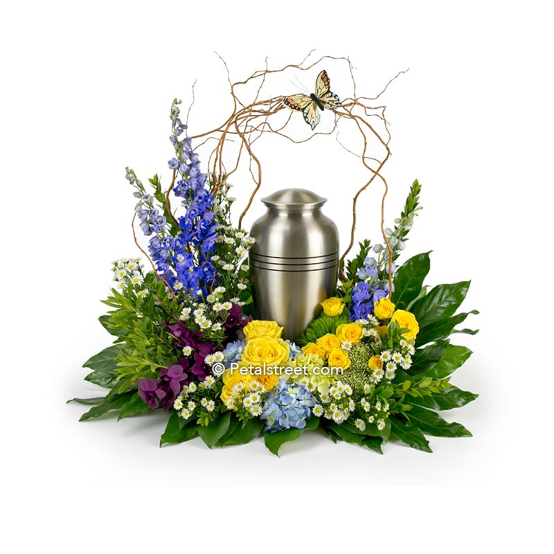 Cremation urn flower arrangement with yellow Roses, blue Delphinium, plum Orchids, decorative Curly Willow arch with a butterfly accent.