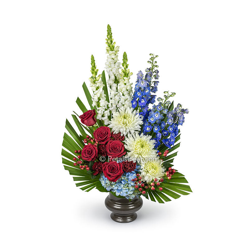 Red, white, and blue funeral basket has Roses, Snap Dragons, Delphinium, Mums, Hydrangea, Carnations, and custom hand-cut foliage.