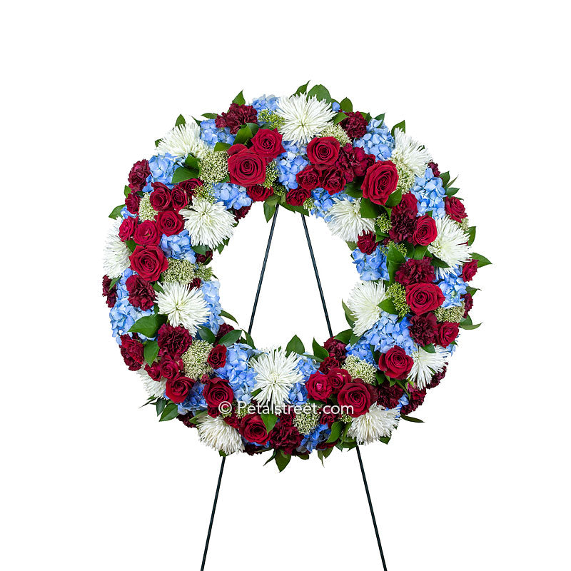 Patriotic red, white, and blue funeral wreath with Roses, Hydrangea, Spider Mums, carnations, and accent foliage.