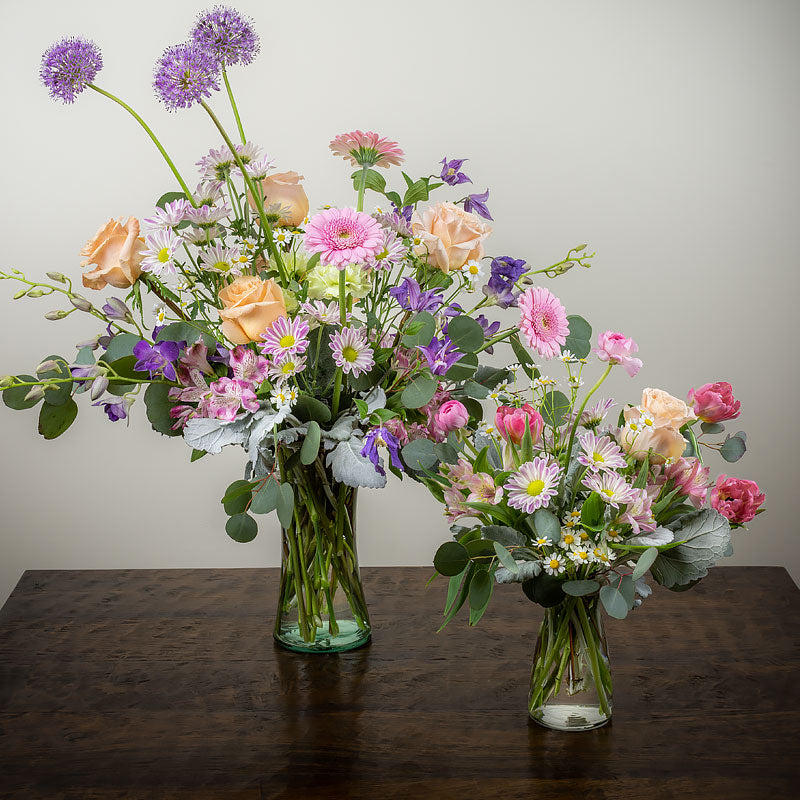 A pair of beautiful soft colored flower arrangements in vases with a mix of Roses, Daisies, Alstromeria, Allium, Clematis, Eucalyptus, and accent foliage