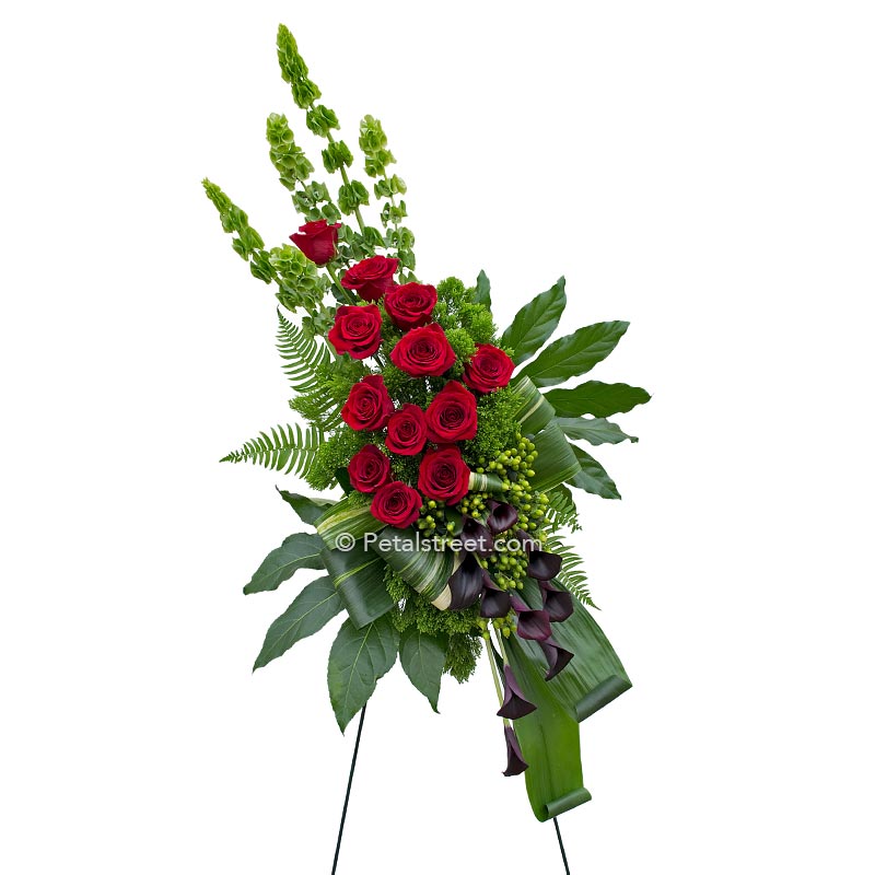 Red Roses and deep plum Calla Lilies arranged with tropical leaves in this standing spray for funeral viewings.