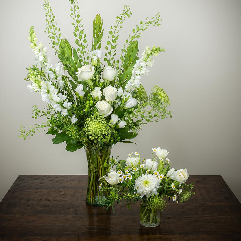 A pair of elegant white and green flower arrangements in vases featuring Roses, Snap Dragons, Lisianthus, Mums, Lace Flower, Bells of Ireland, and accent greenery at Petal Street Flower Company florist