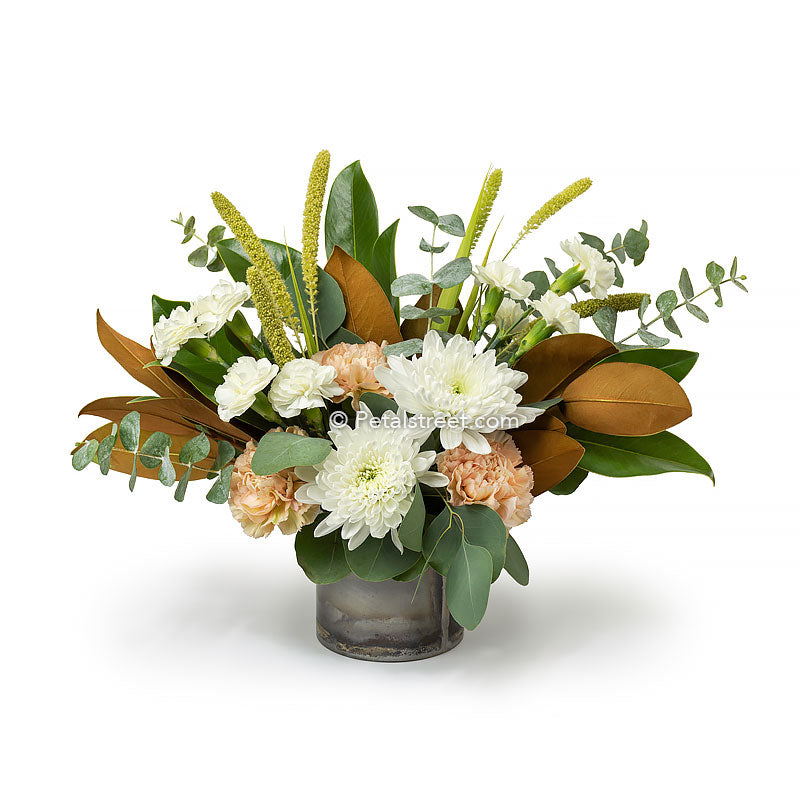 Fall flower arrangement with white mums, white mini carnations, soft peach carnations, millet, Eucalyptus and Magnolia leaves arranged in a rustic tin cylinder.