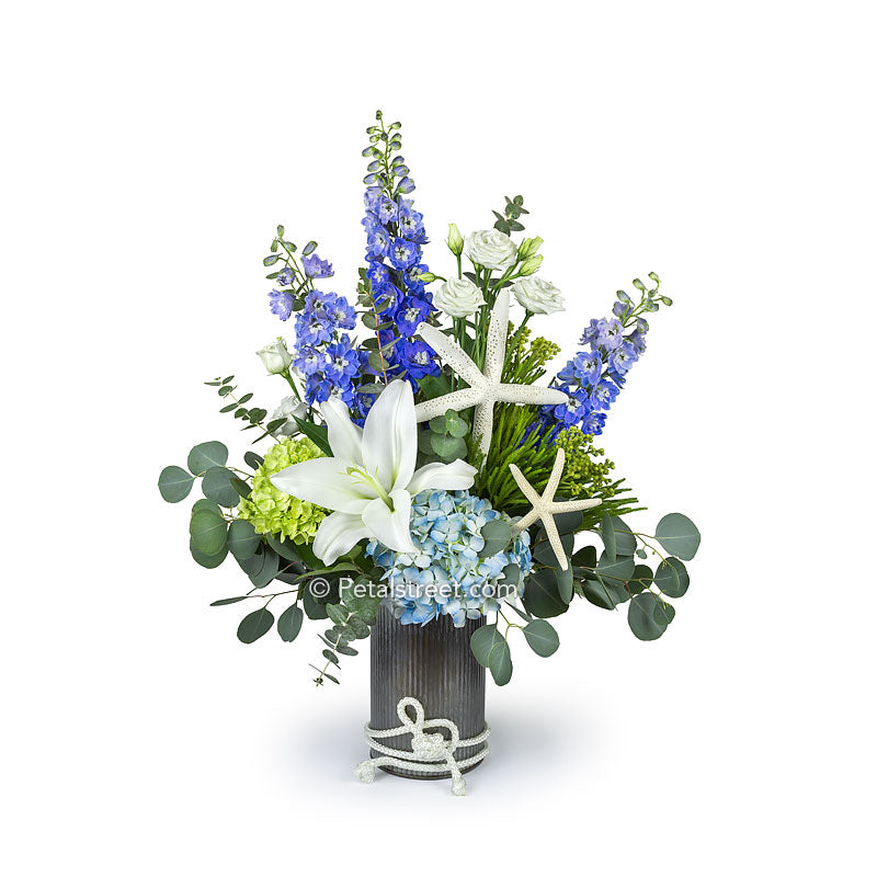 Beach flowers or nautical flowers with Lilies, Hydrangea, Delphinium, Eucalyptus, and Starfish in a tin container with rope accent.