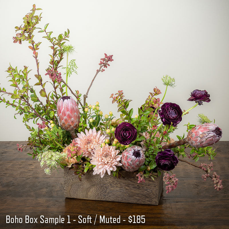 Beautiful bohemian flower arrangement with soft colors in a rustic wood garden box featuring Protea, Ranunculus, Lace Flower, Mums, and accents branches at Petal Street Flower Company florist