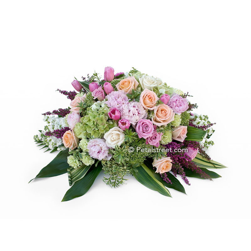 Casket spray with soft pink Peonies, peach Roses, mini green Hydrangea, and Ti Leaf accents.