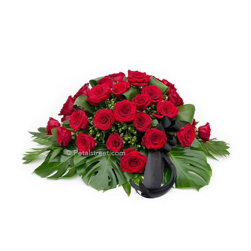 Modern red Rose casket spray with lush tropical leaves.