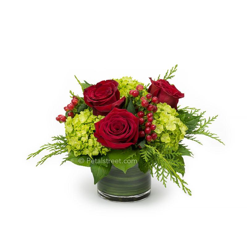 a short cylinder vase with red Roses, green mini Hydrangea, red Hypericum Berries, and seasonal greens, Merry Christmas!