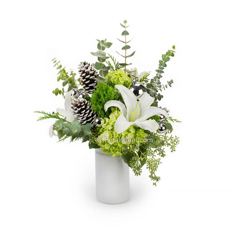 White and green holiday flower arrangement with Lilies, Trachelium, Hydrangea, frosted Pine Cones, Eucalyptus, and silver ornaments.