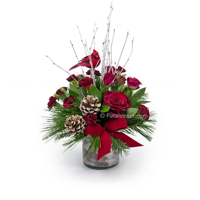 Christmas flower arrangement with red Roses and mini spray Carnations in holiday greens with a  Cardinal bird perched in Birch twig accents.