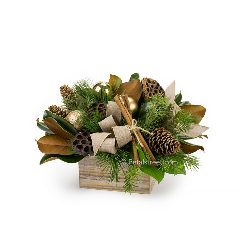 Holiday arrangement in a wood box with Pine and Spruce branches, Magnolia Leaves, Lotus Pods, Pine Cones, Cinnamon Sticks, and gold holiday ornament accents.