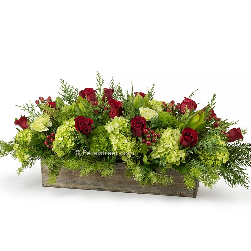 Extra long low Christmas table arrangement with a mix of seasonal greenery, beautiful red Roses,  and red Hypericum accents arranged in a warm wood box by Petal Street Flower Company florist