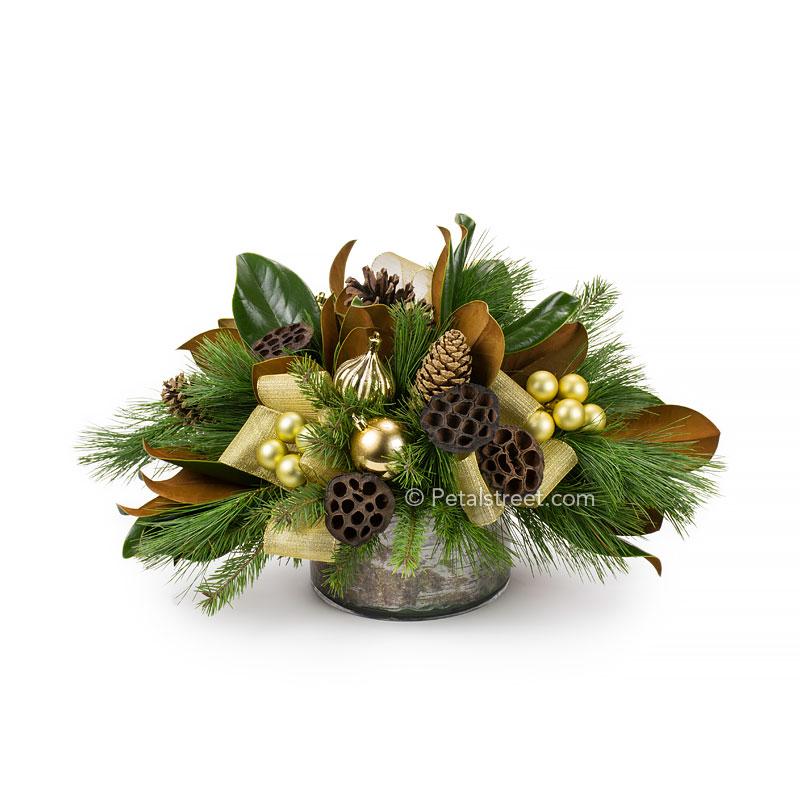 Christmas table centerpiece with Magnolia Leaves, a variety of seasonal greenery, dried Lotus Pods, Pine Cones,  and a mix of gold holiday ornaments.