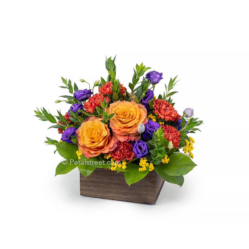 Orange Roses and Carnations with purple Lisianthus, yellow Tansey, and accent foliage in a weathered wood box.