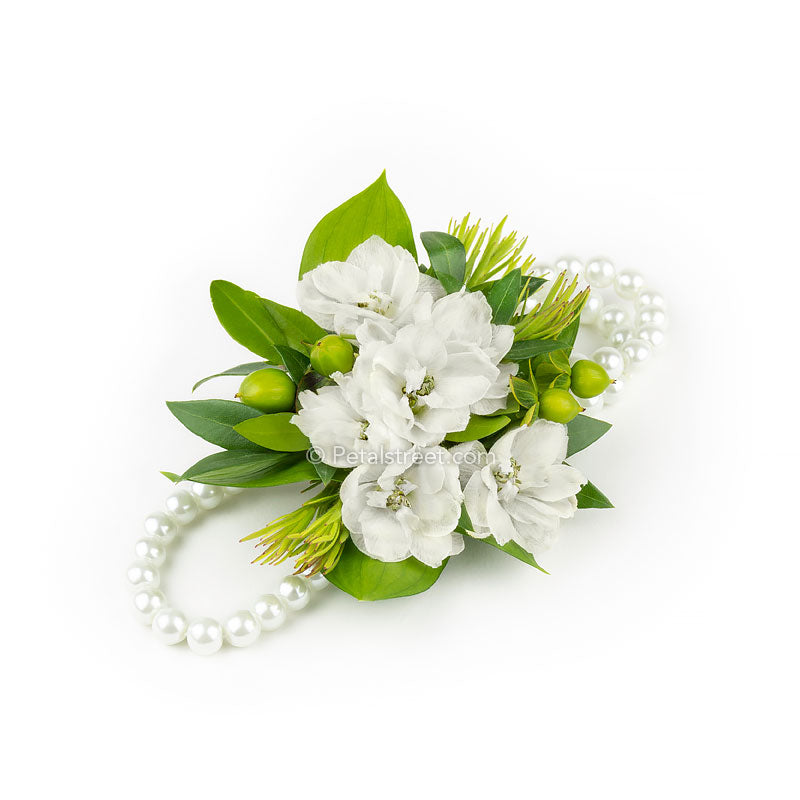 Wearable flower wristlet with white Delphinium blooms greenery accents on a pearl bracelet by Petal Street Flower Company