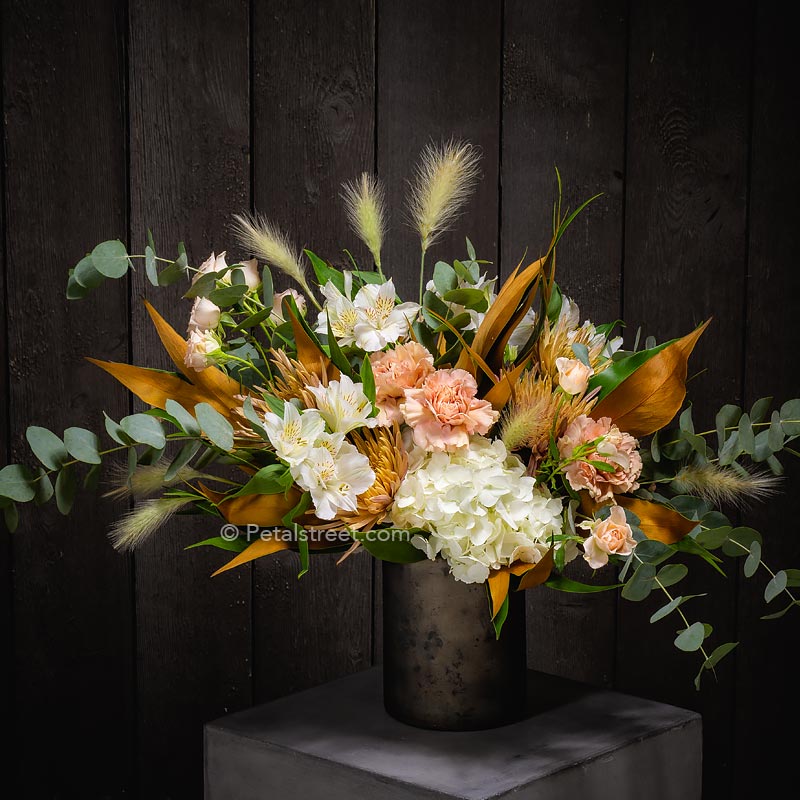 Upscale contemporary flower arrangement with hydrangea, dianthus, alstroemeria, Eucalyptus, and warm Grevillea in a metal cylinder vase.