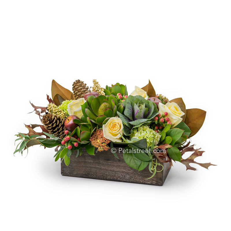 A rustic wood box with a mix of yellow Roses, Kale, Berries, mini Hydrangea, and Pine Cones accented with Magnolia and Oak Leaves.