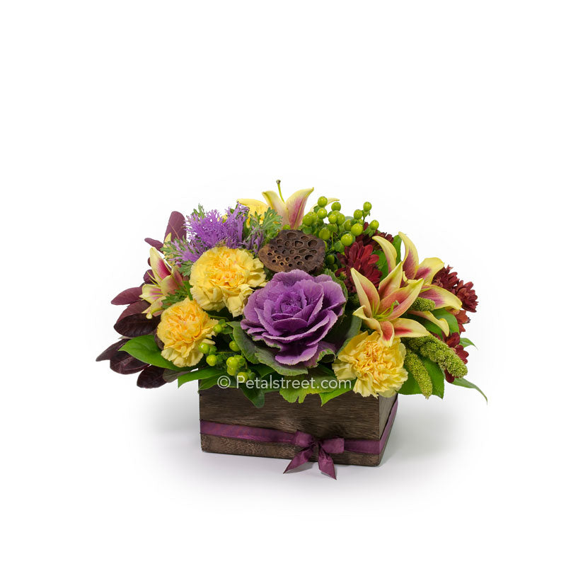 Vibrant mixed Fall flowers such as purple Kale, yellow Lilies and Carnations, red Mums, and green Berry accents in a wood box.