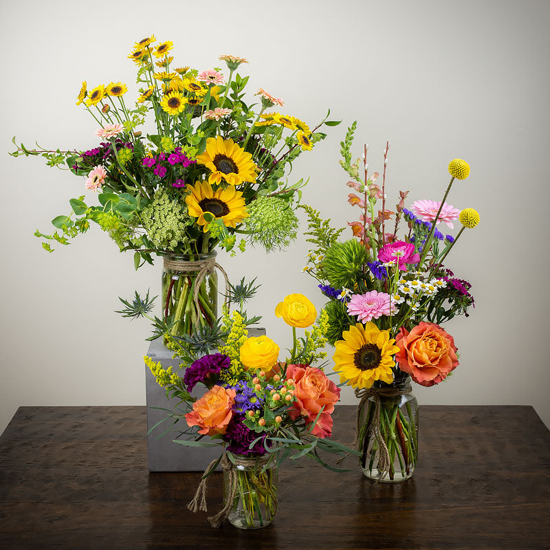 Group of three mason jar flower arrangements, small, medium, large, made with vibrant colored flowers and textures at Petal Street Flower Company florist
