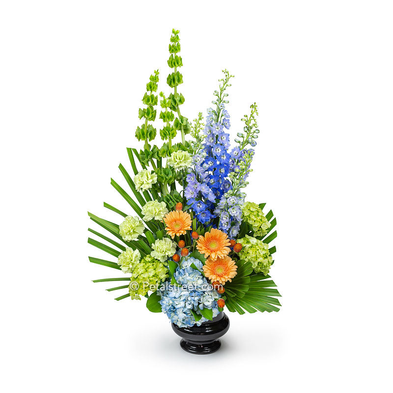 Funeral basket with peach Gerbera Daisies, blue hydrangea and Delphinium, green Carnations, and Bells of Ireland.