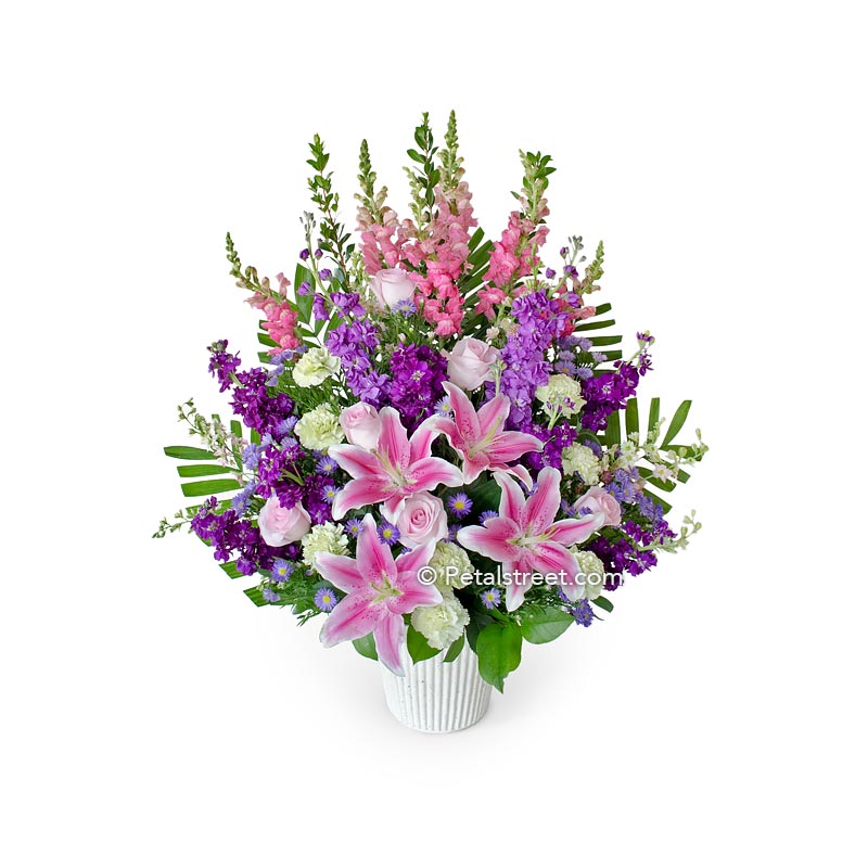 Pink, purple, and white funeral basket with Lilies, Roses, Snapdragons, Stock, Carnations, Hydrangea, and accent greenery.