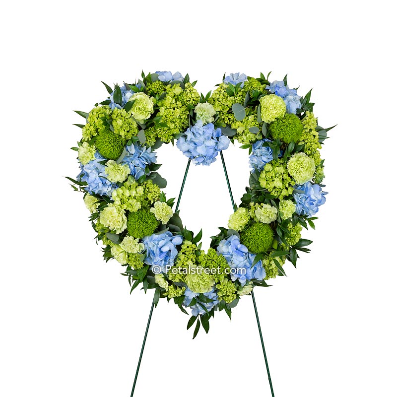 Beautiful blue and green funeral heart wreath with a mix of Hydrangea, Carnations, Green Trick, and foliage accents.