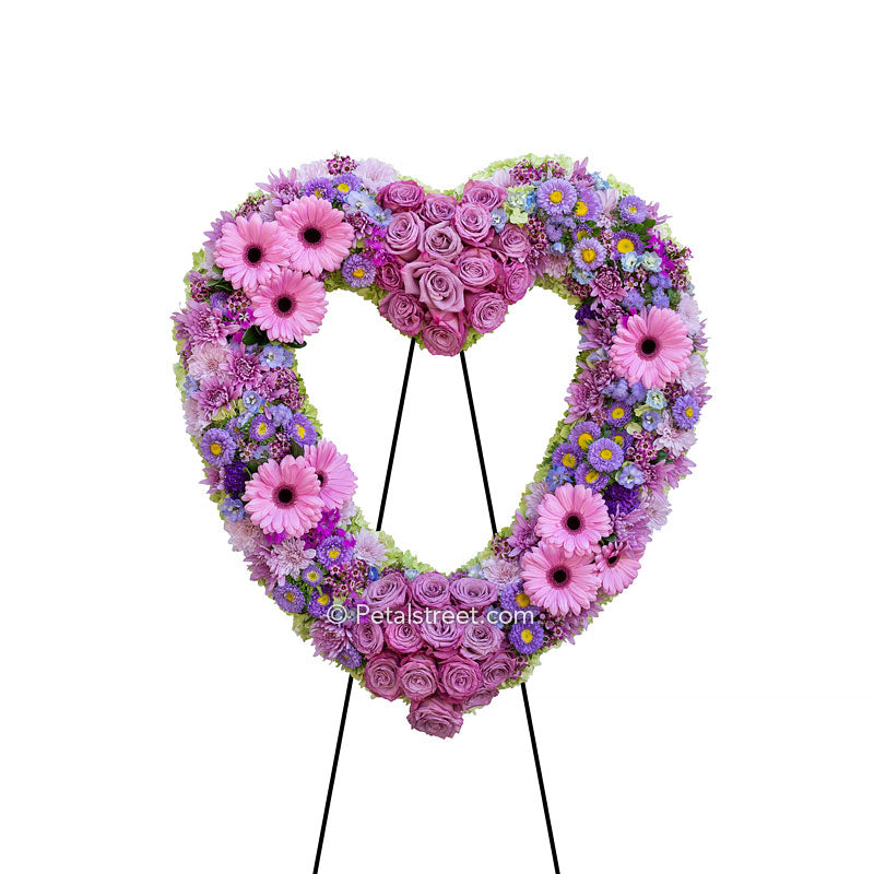 A flower abundant funeral heart form, with a variety of soft pinks and purples, includes Roses, Gerbera Daisies, large Asters, and a mix of accent flowers.