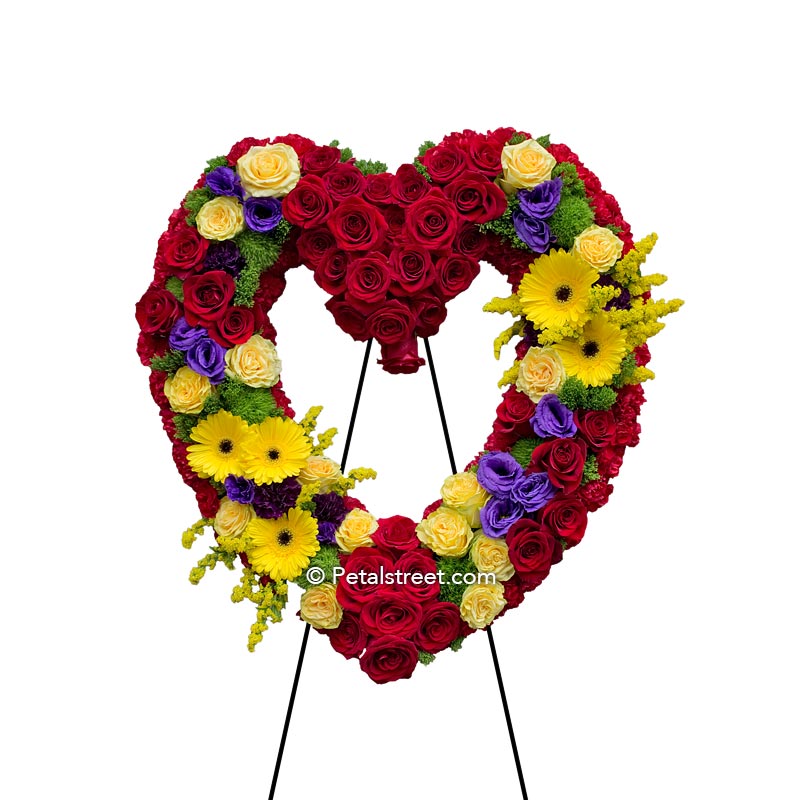 Vibrant funeral flower heart form with red Roses, yellow mini Roses, yellow Gerbera Daisies,  Solidago, and Lisianthus.