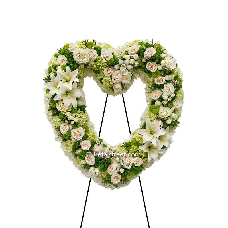 All white funeral flower heart form with Roses, Lilies, and Orchids accented with green Carnations, Green trick, and foliage touches.