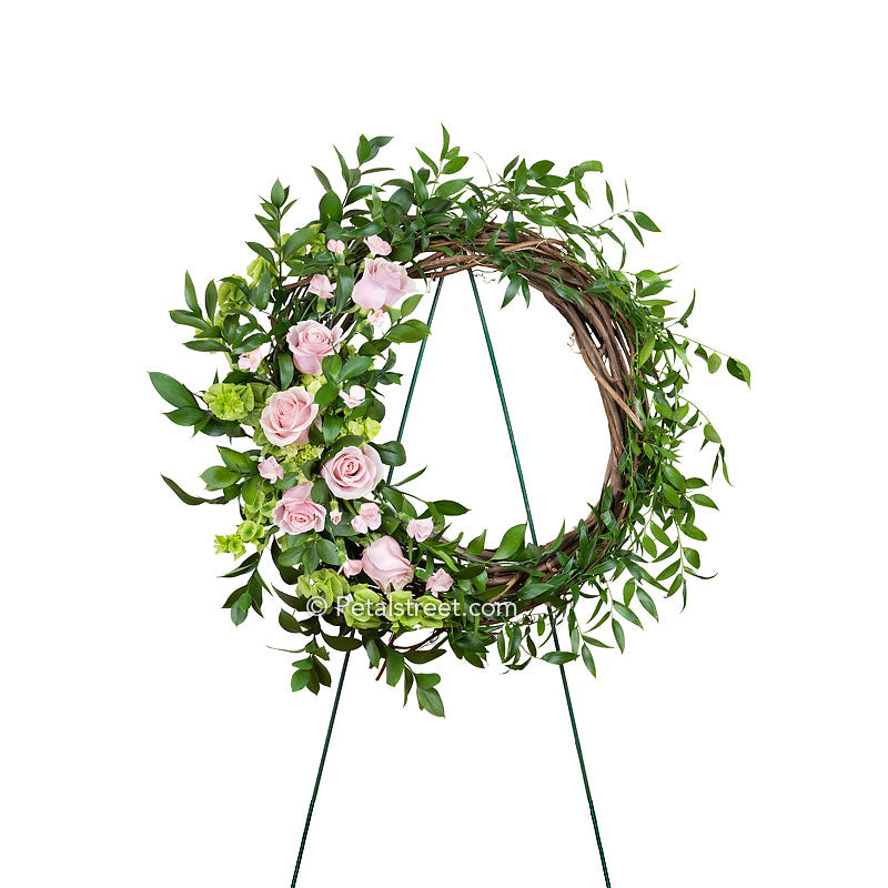 Grapevine and foliage funeral wreath with pink mini Gerbera Daisies, purple Aster, green mini Hydrangea, Snap Dragons, and Solidago.