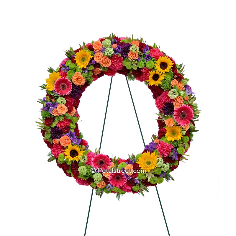 Vibrant funeral wreath with Sunflowers, Gerbera Daisies, Roses, and mixed accents.
