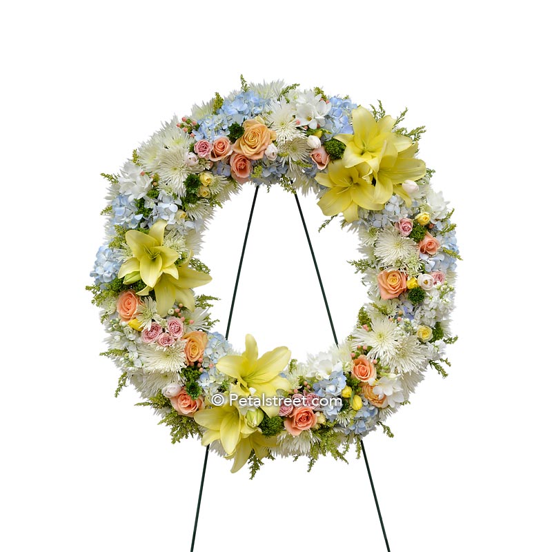 Funeral wreath with mixed flowers in soft colors such as yellow, peach, and white.