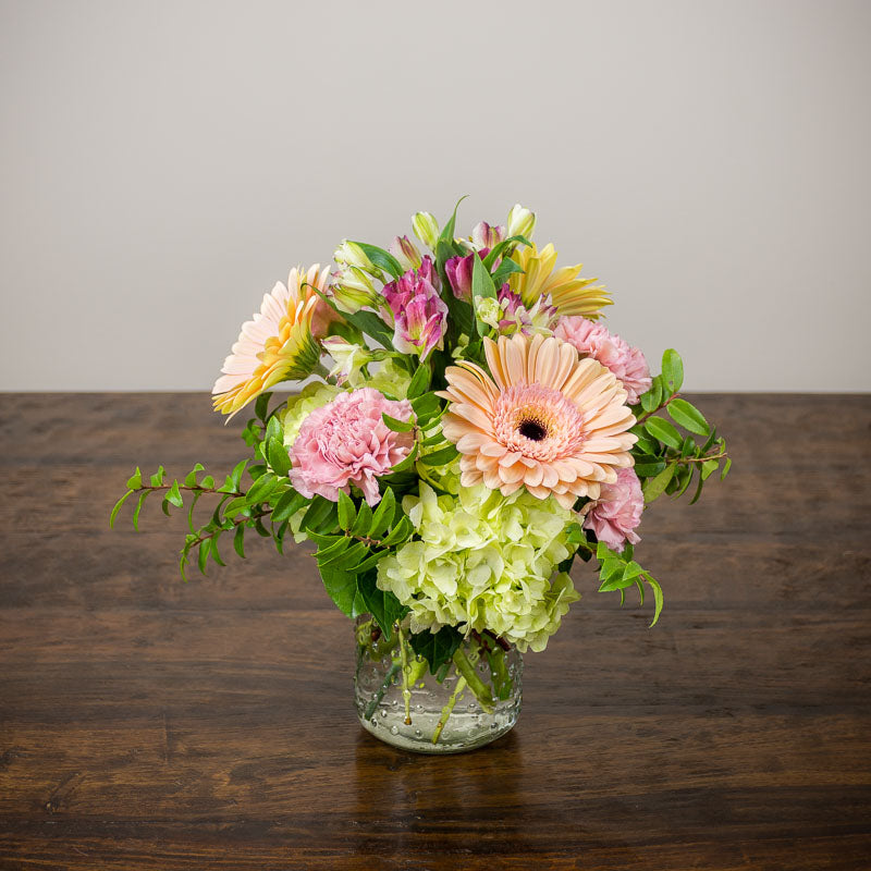 Cylinder vase of flowers with Gerbera Daisies, Hydrangea, and accent blooms and foliage.