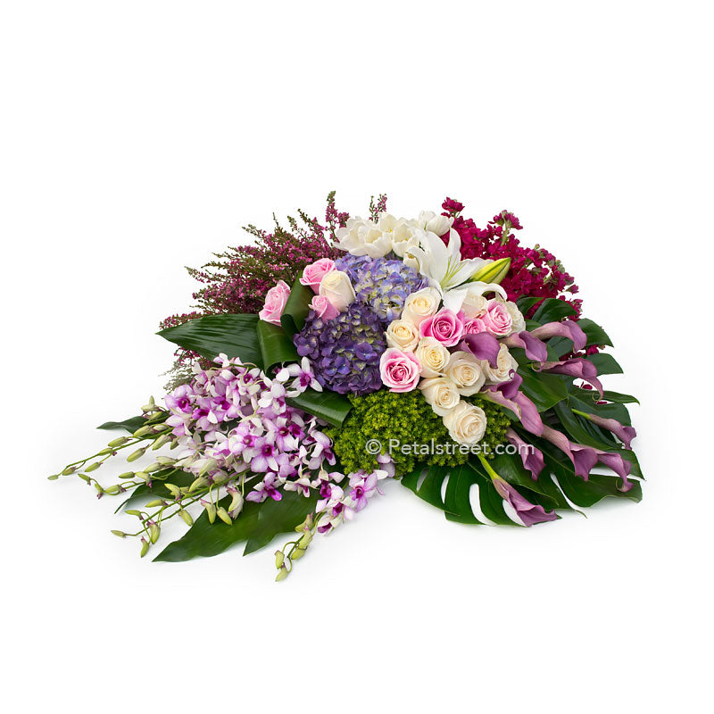 Gorgeous family casket spray with pink and white Roses, Hydrangea, Orchids, plum Calla Lilies, and lush tropical leaves.