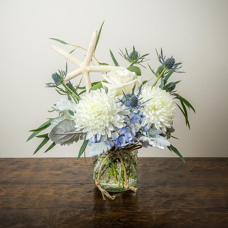 Nautical beach themed flower arrangement with white Mums, blue Hydrangea, blue Thistle accents and driedStarfish in a Hobnail Jar by Petal Street Flower Company florist in Point Pleasant NJ
