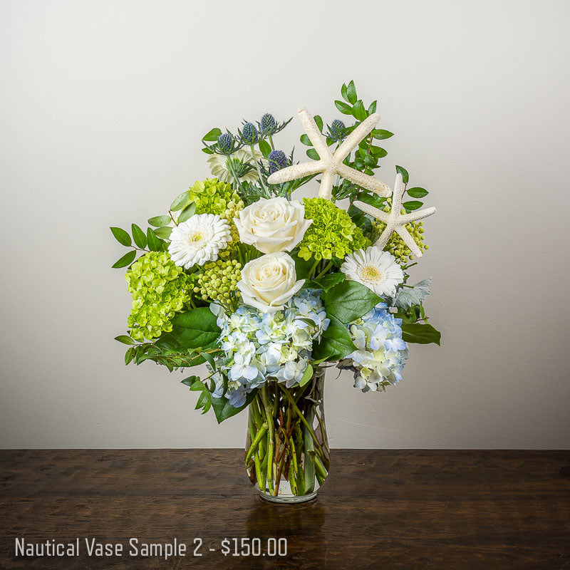Beach themed vase arrangement with white Roses and Gerbera Daisies, blue Hydrangea, blue Thistle accents and dried Starfish in a tall vase by Petal Street Flower Company florist in Point Pleasant NJ