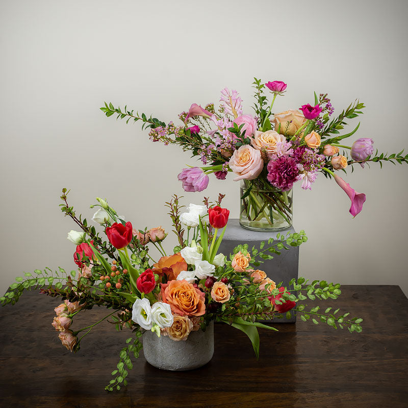 A pair of colorful flower arrangements in a loose whimsical style featuring Ranunculus, Lisianthus, Roses, Tulips, Cala Lilies, and assorted accent foliage at Petal Street Flower Company Florist
