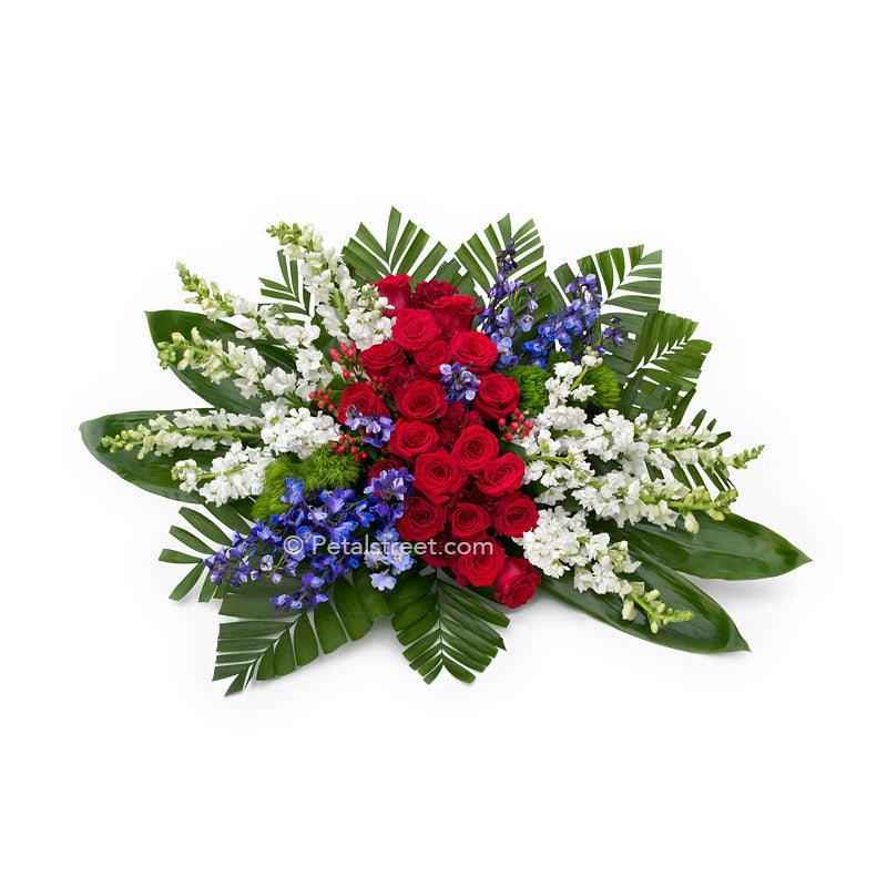 Special red, white, blue casket spray for family funeral features Roses, Delphinium, Snapdragons, and accent foliage.