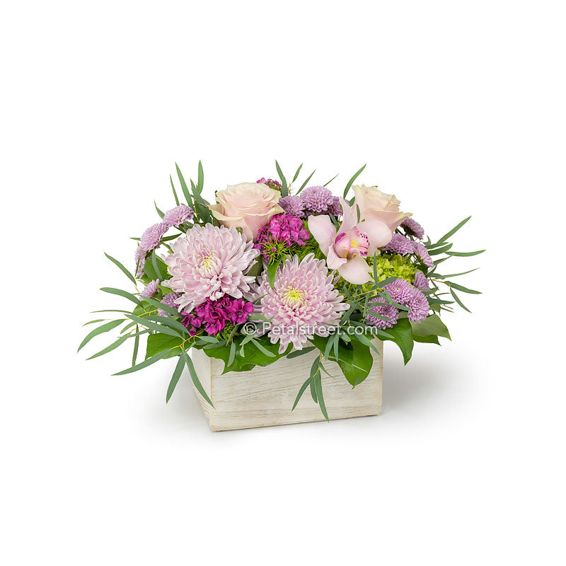 Mixed pink flowers arranged in a white wood box such as Roses, Orchids, Sweet William, Mums, and Eucalyptus