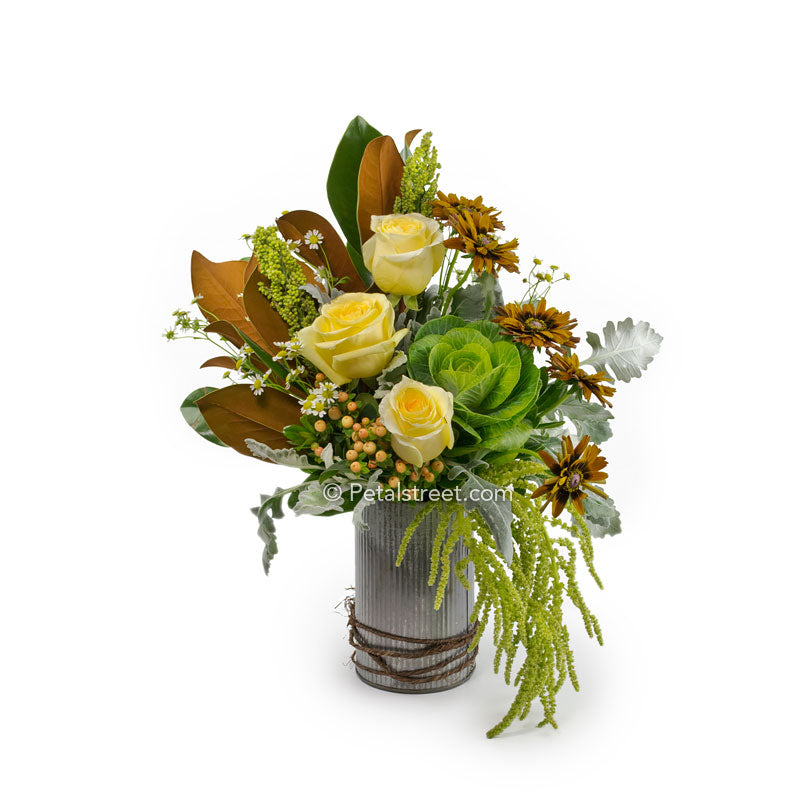 Rustic cylinder tin with bright yellow Roses, Kale, brown Mums, Berries, and Magnolia leaves for the Autumn season.