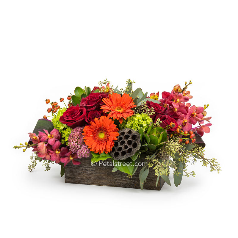 Rustic Fall Flower arrangement with red Roses, orange Gerbera Daisies, red Orchids, green mini Hydrangea, orange Alstroemeria, and Eucalyptus arranged in a box.