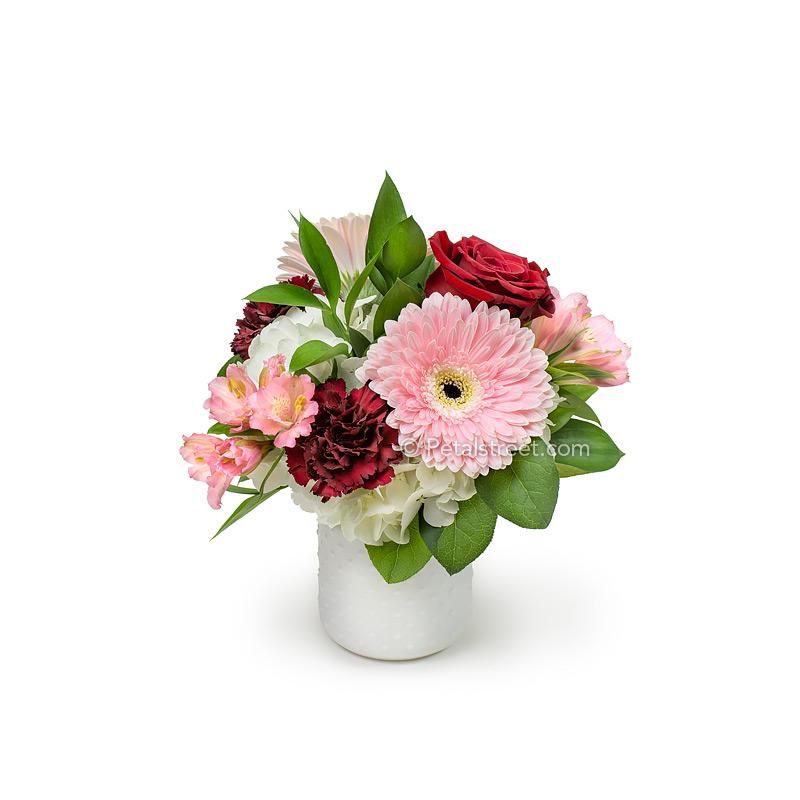 Valentine's Day flowers by Point Pleasant Florist Petal Street Flower Company has pink Gerber Daisies and Alstroemeria, red Roses and Carnations, white Hydrangea, and accent foliage arranged in a white hobnail jar. Classy and charming.