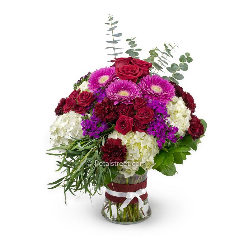 Large bouquet of flowers in a vase with red Roses, pink Gerbera Daisies, burgundy Carnations, pink Sweet William, white Hydrangea, and Eucalyptus foliage.